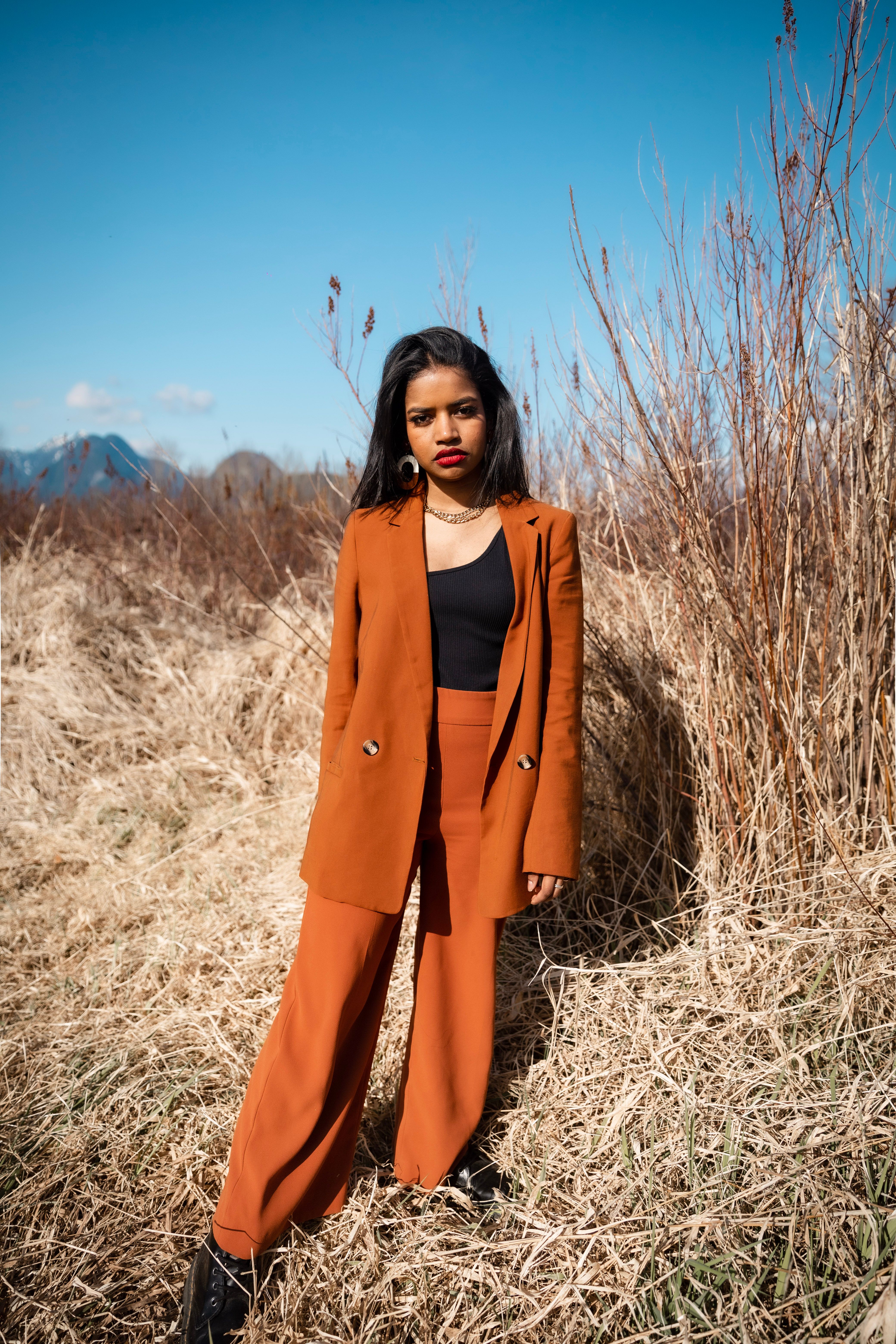 A Woman in Brown Blazer Standing on a Dried Grass Field · Free Stock Photo