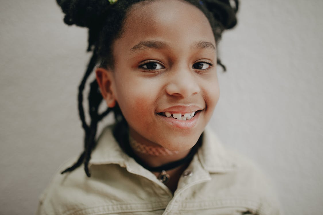 A young girl with dreadlocks smiles brightly, radiating joy and positivity in her expression.