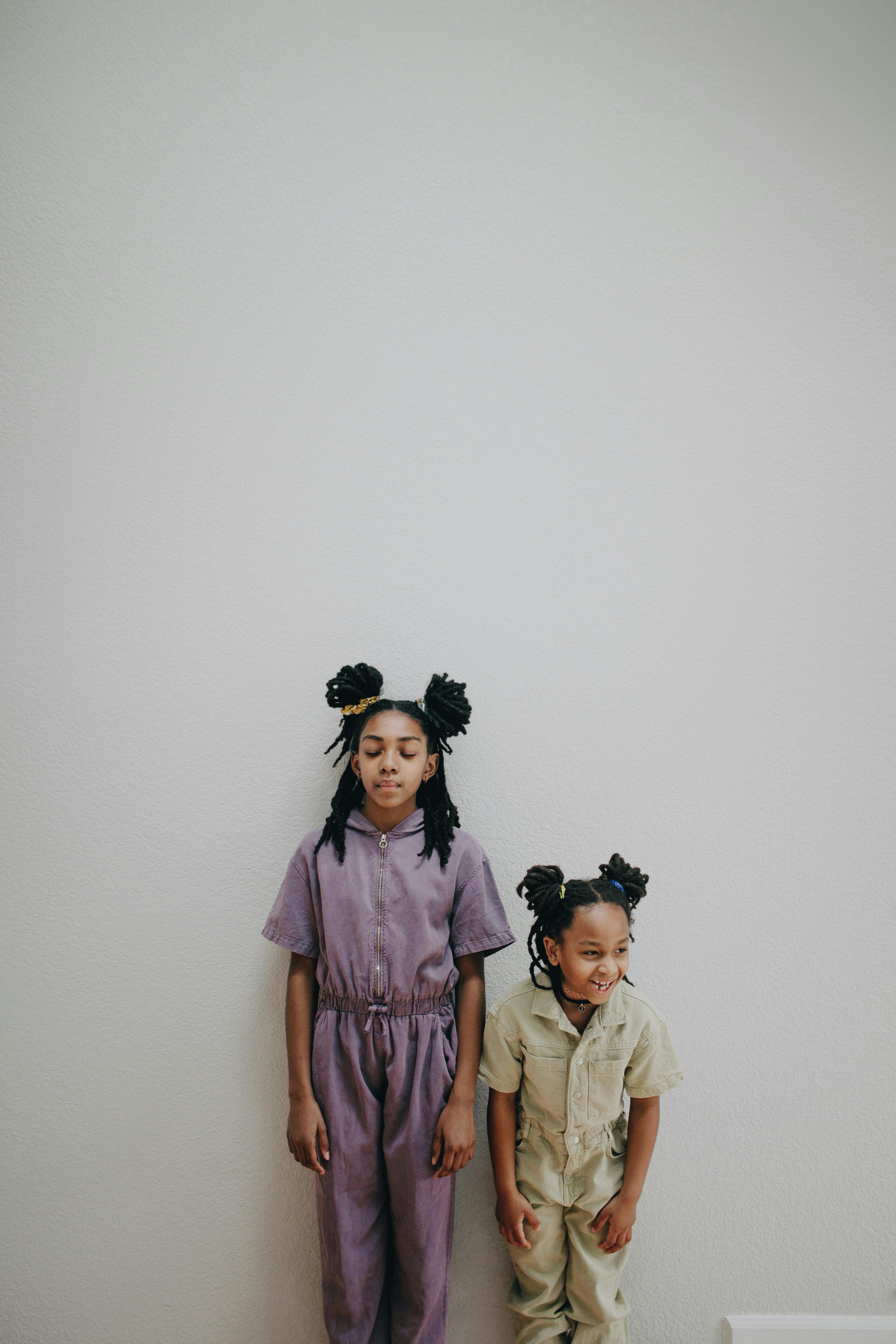 Charming studio shot of joyful African American sisters posing stylishly against a white background.