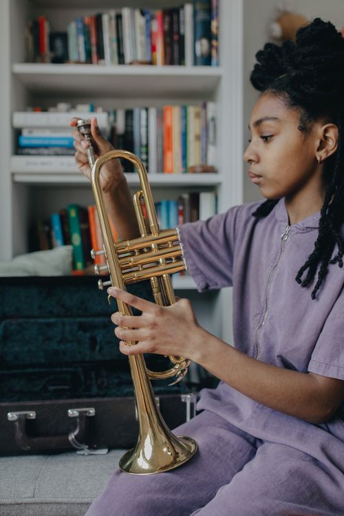 Free Black woman with trumpet in cozy room, focused on music preparation. Stock Photo