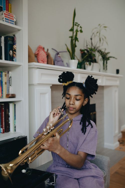 Free A young girl seated indoors, practicing the trumpet in a cozy home setting. Stock Photo