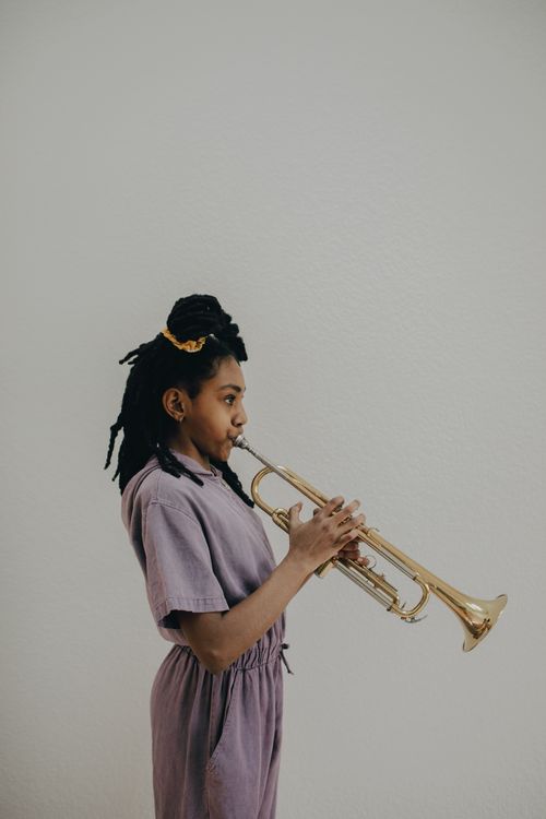 Free A young female musician passionately playing the trumpet against a gray wall. Stock Photo