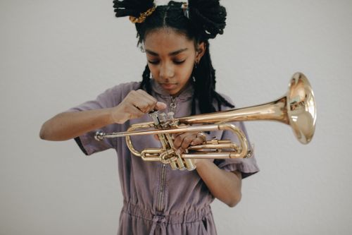 Free A young girl focuses on playing a brass trumpet during a studio photoshoot. Perfect for music-related themes. Stock Photo