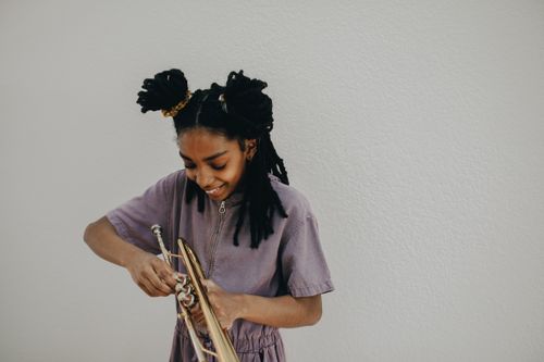Free A young woman with dreadlocks smiling as she plays the trumpet indoors. Stock Photo