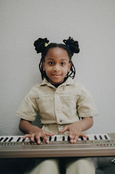 A young girl with afro hair plays an electric keyboard indoors, showcasing musical interest.