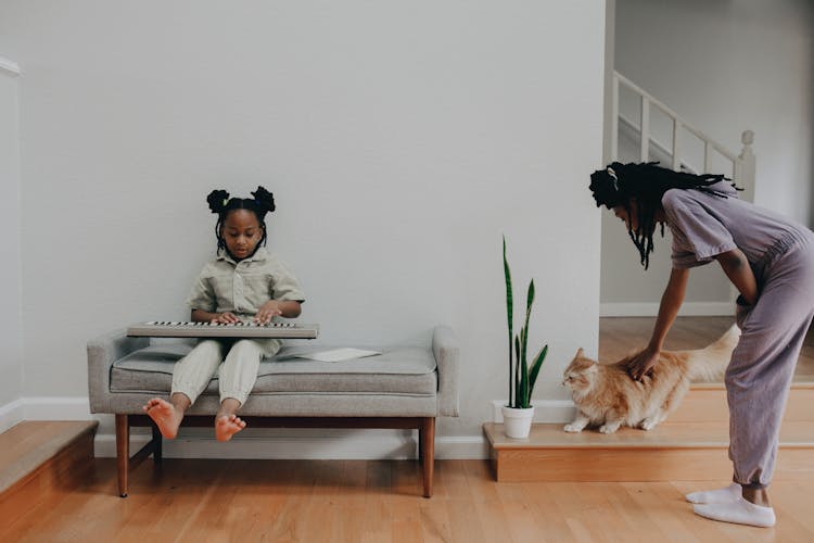 A Child Playing An Electronic Keyboard And A Girl Petting A Cat