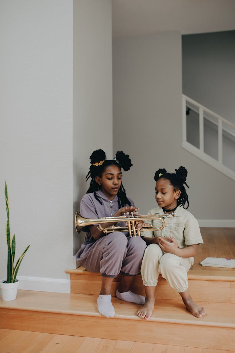 A Girl Teaching Her Sister How To Play The Trumpet At Home