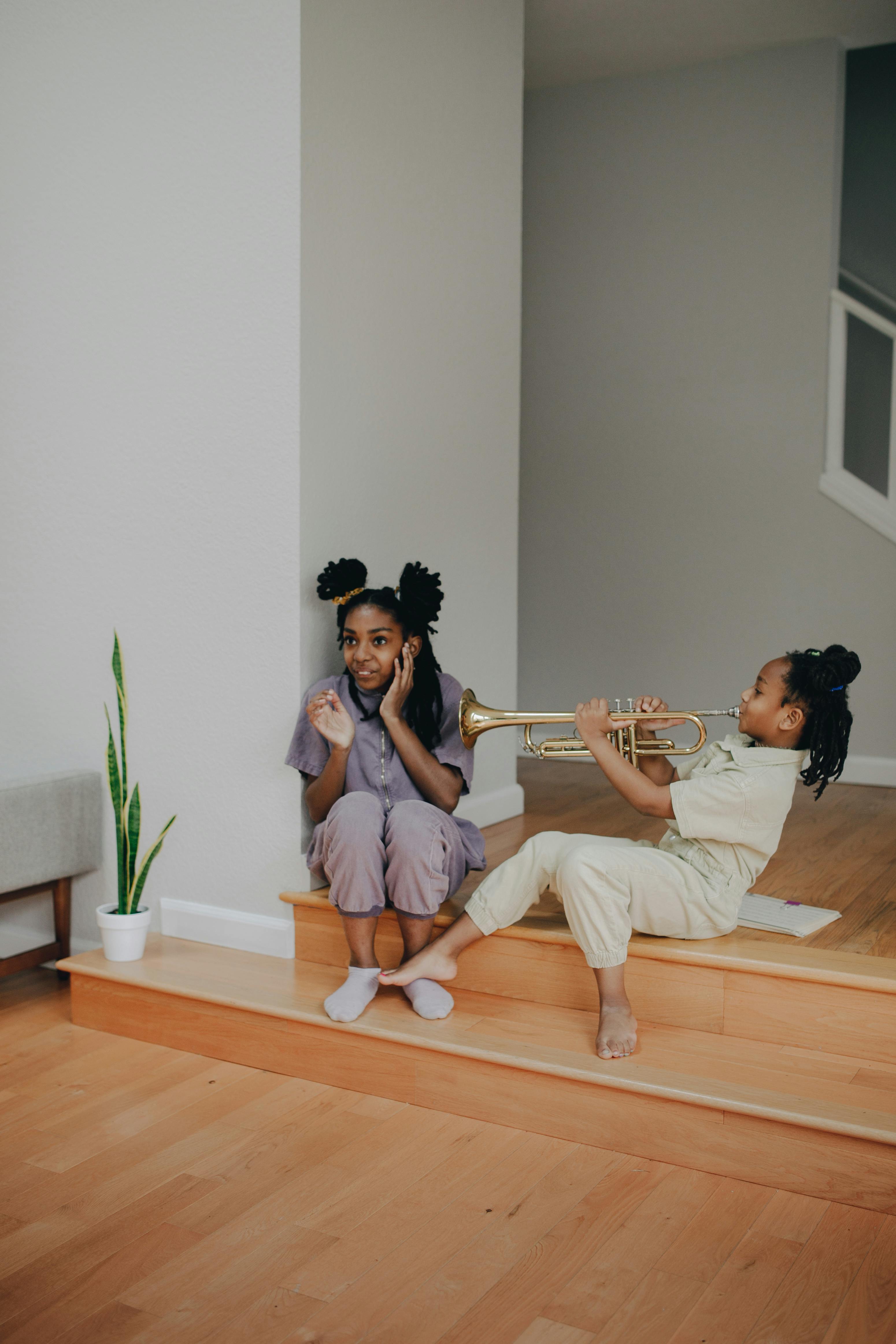 Two African American girls playing with a trumpet indoors, creating a joyful atmosphere.