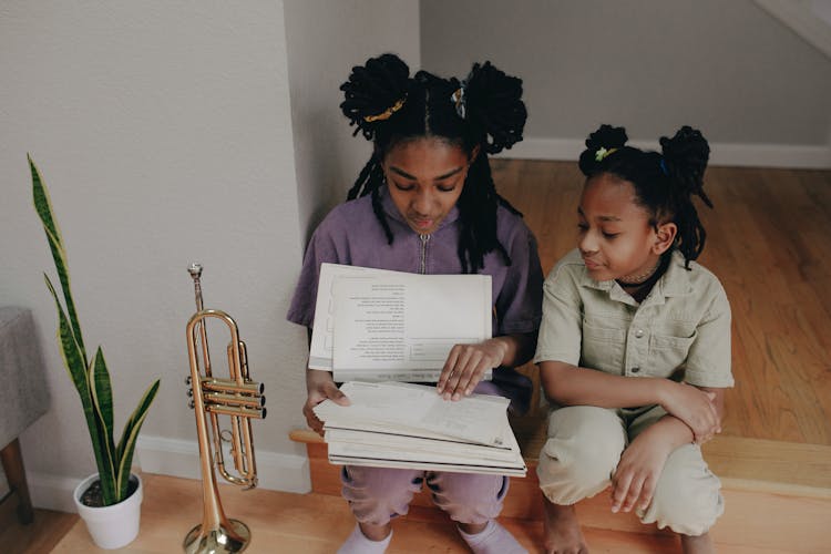 Sisters Looking At Papers Together While Sitting On The Floor