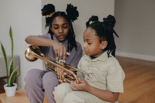 Free Two children sitting indoors, one teaching the other to play a brass trumpet, creating a warm family moment. Stock Photo