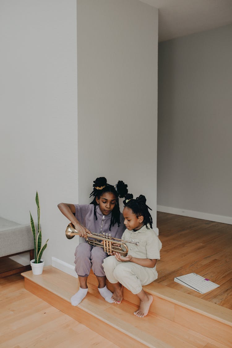 A Girl Teaching Her Sister How To Play The Trumpet At Home