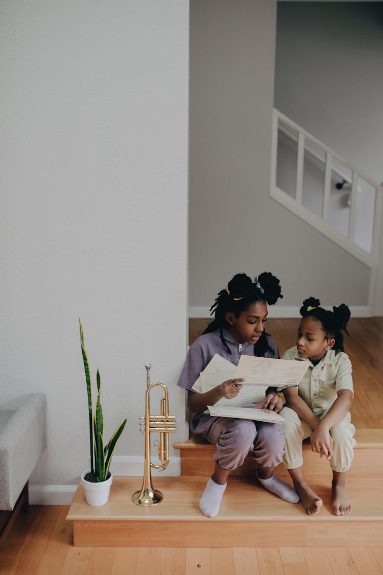 Sisters Looking At Papers Together While Sitting On The Floor