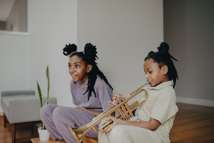 A Girl Playing The Trumpet Beside Her Sister