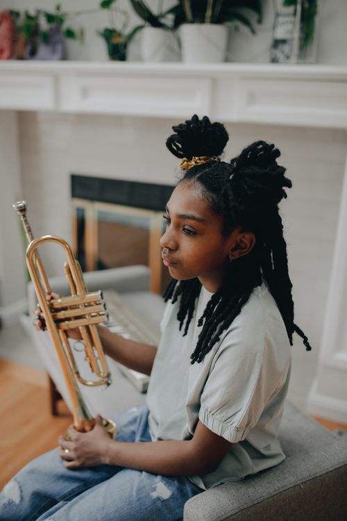Free African American girl holding a brass trumpet in a cozy indoor setting. Stock Photo