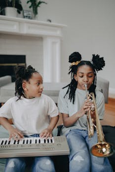 Two young girls playing keyboard and trumpet, enjoying music indoors.