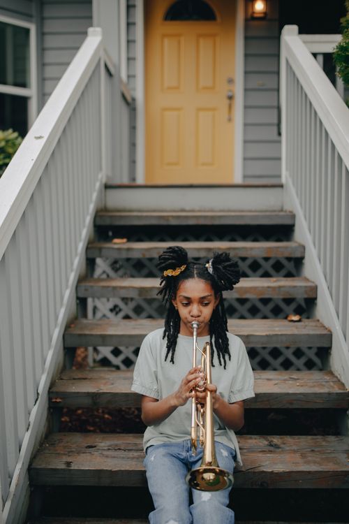 Free A young girl playing a trumpet while sitting on porch steps Stock Photo