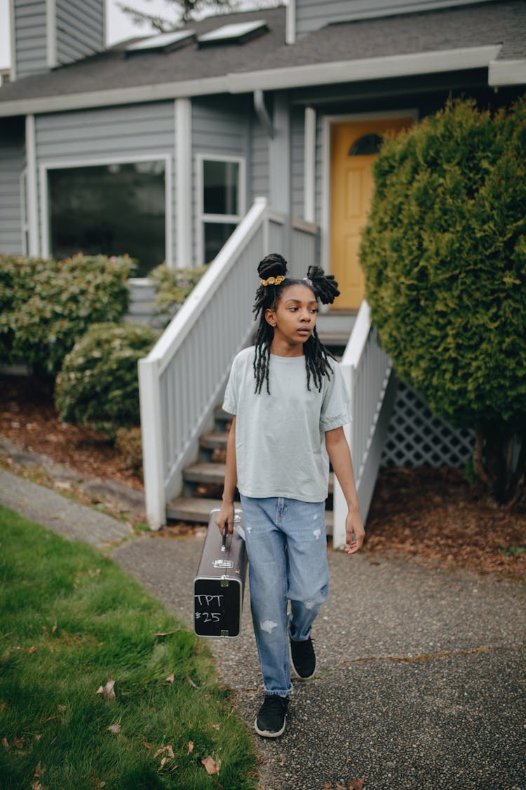 A Young Girl Walking While Carrying A Suitcase