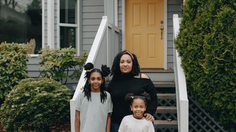 A joyful family standing together in front of their house with a yellow door, exuding warmth and happiness.