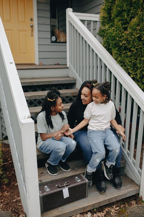 Free A mother and her daughters bond on the house steps, sharing a joyful moment together. Stock Photo