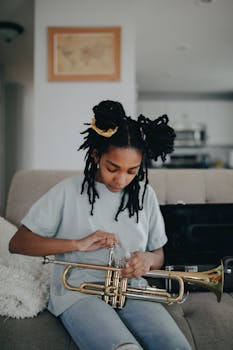 Young black girl with dreadlocks assembling a trumpet indoors in a cozy home setting.