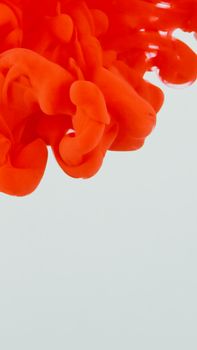 Close-up of a vibrant red paint swirl creating abstract patterns against a white backdrop.