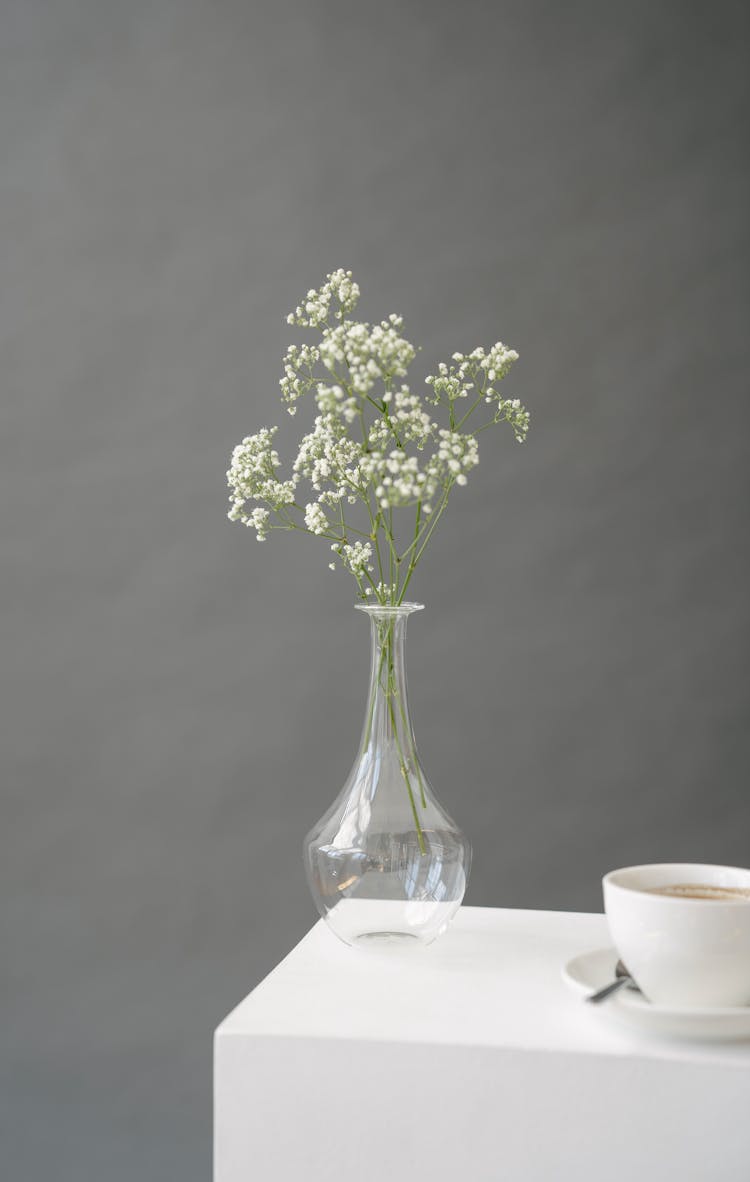 Vase With Fresh Flowers On Pedestal Near Cup Of Coffee