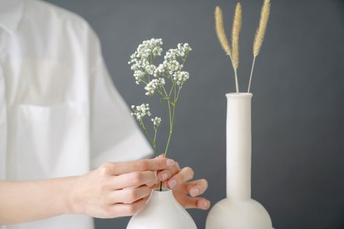 Free Crop unrecognizable female in white clothes putting thin white twigs in ceramic vase against gray background in modern light room Stock Photo