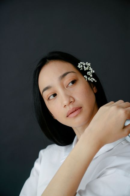 Attractive Asian female in white wear and small twig in hair looking away while standing on gray bac