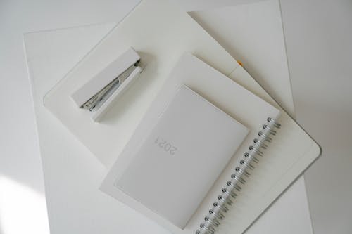 White colored diary with notebook and stapler located on planner