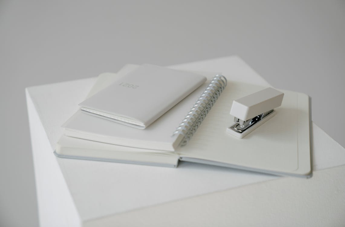 Notepad with stapler and diary with planner on white cube