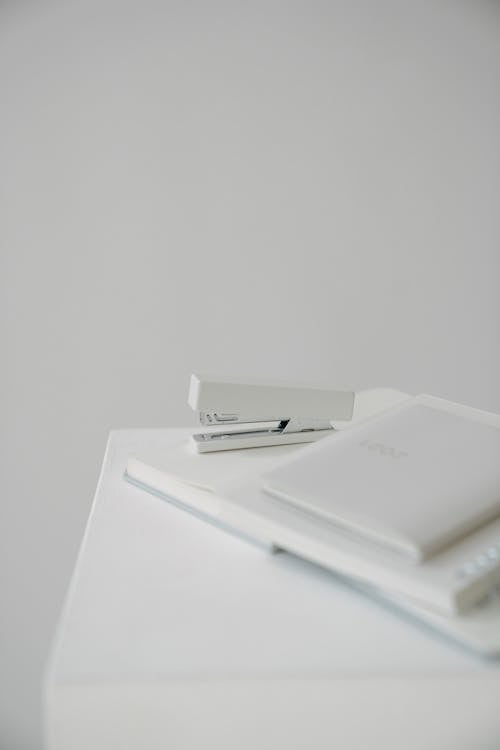 High angle of stapler with blurred stationery placed on white surface against blank wall
