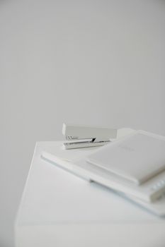 High angle of stapler with blurred stationery placed on white surface against blank wall