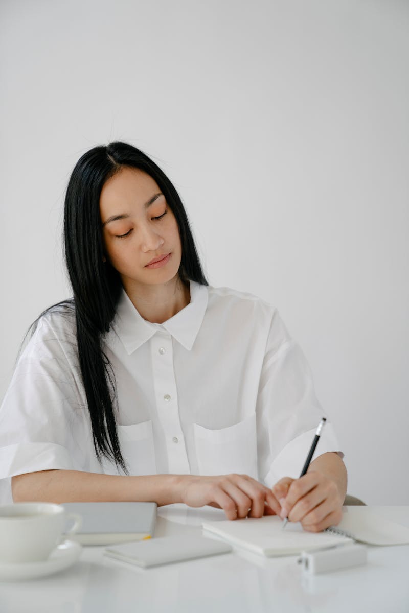 Ethnic female student writing in notebook on white table