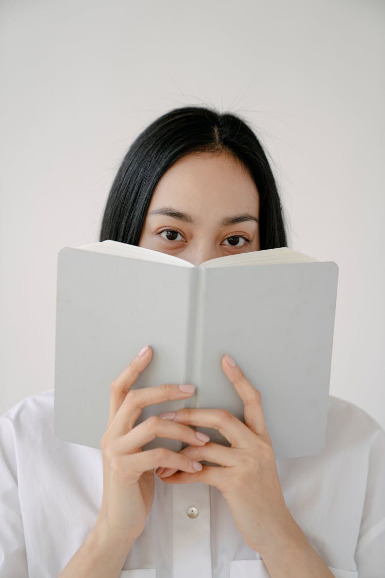 Ethnic Woman Hiding Face Behind Book Against White Background