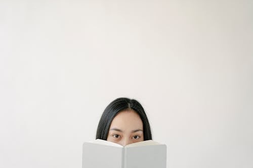 Blank wall with upper part of Asian woman face hidden behind white book