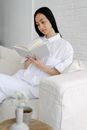 Serious Asian woman reading book on sofa near table