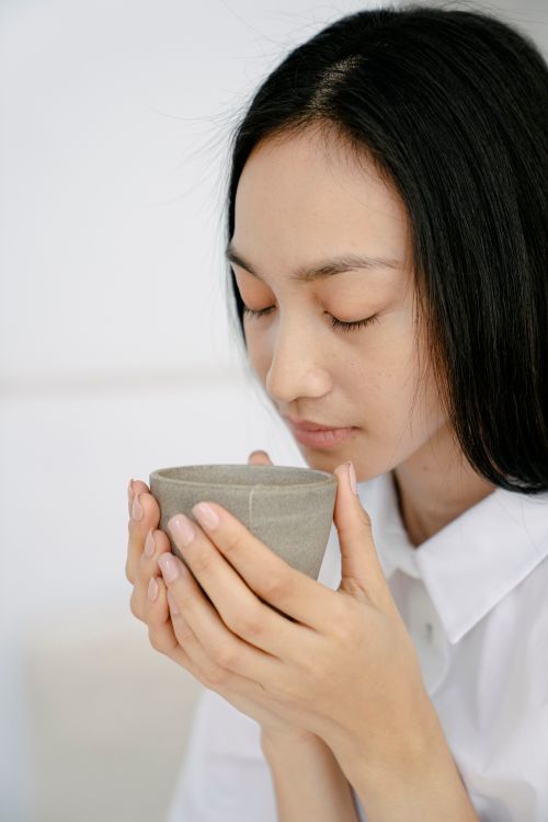 Free Serene ethnic female with long dark hair and closed eyes smelling aromatic hot tea in cup Stock Photo