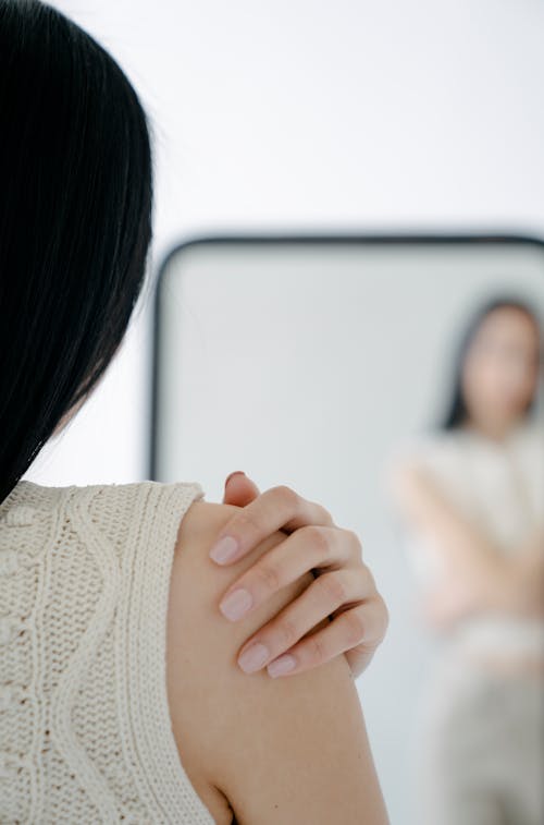 Free Woman touching shoulder while standing near mirror Stock Photo