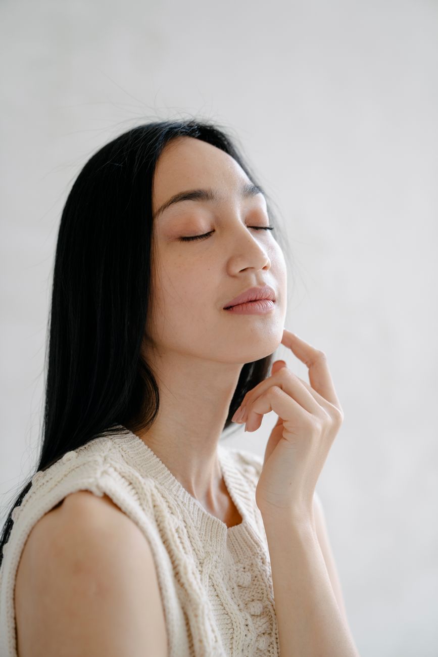 Side view of serene Asia female with long dark hair wearing white sleeveless shirt gently touching c