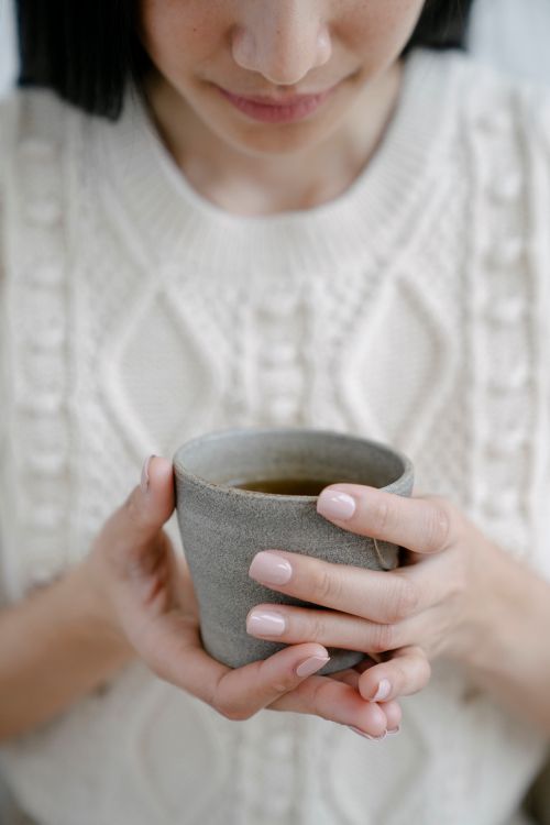 Free Crop female in white knitted wear with ceramic cup of hot aromatic tea for teatime Stock Photo