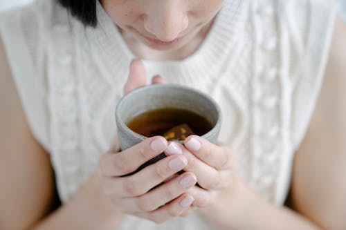 Free High angle of crop female smelling aromatic freshly brewed tea in ceramic cup Stock Photo