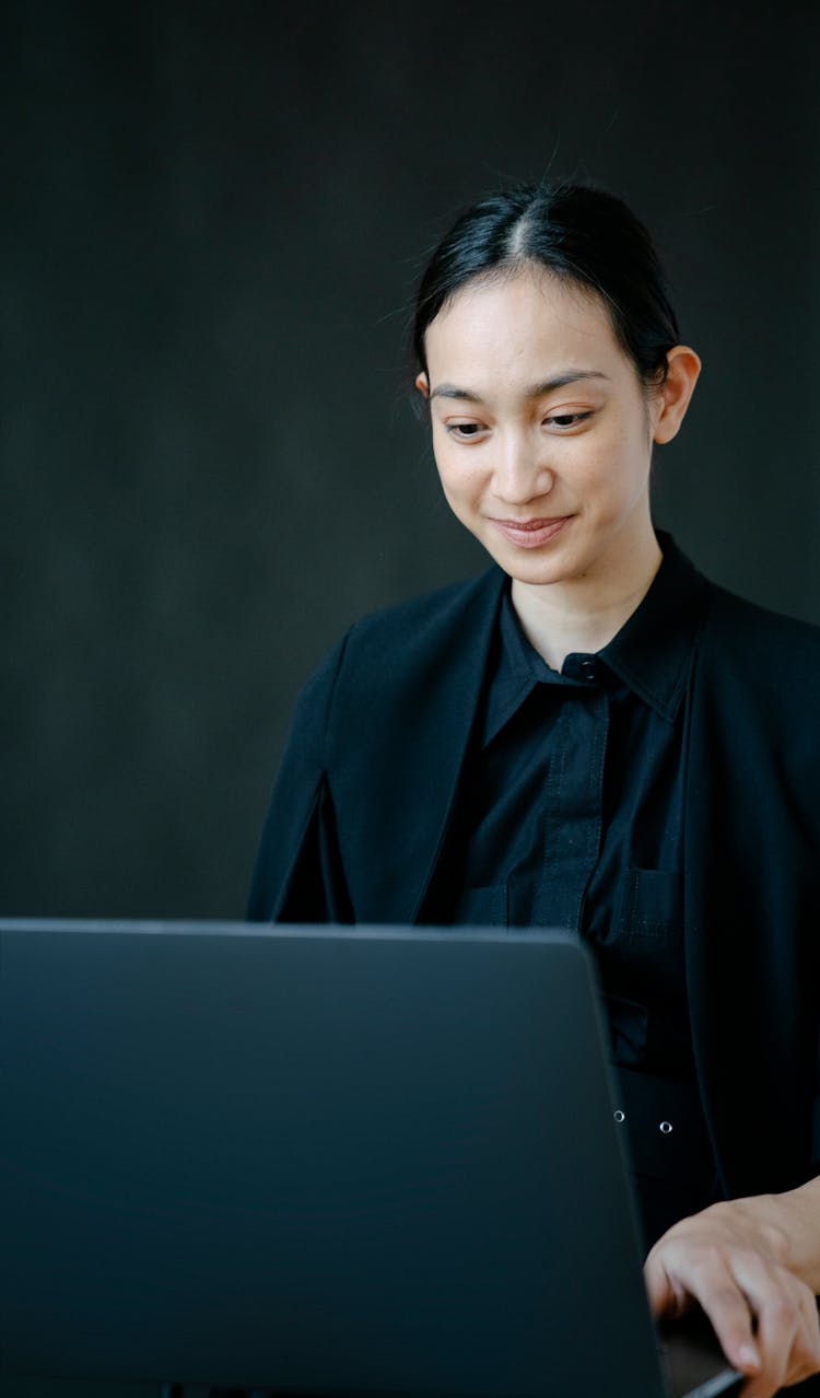 A Woman In Black Blazer Looking At Her Laptop