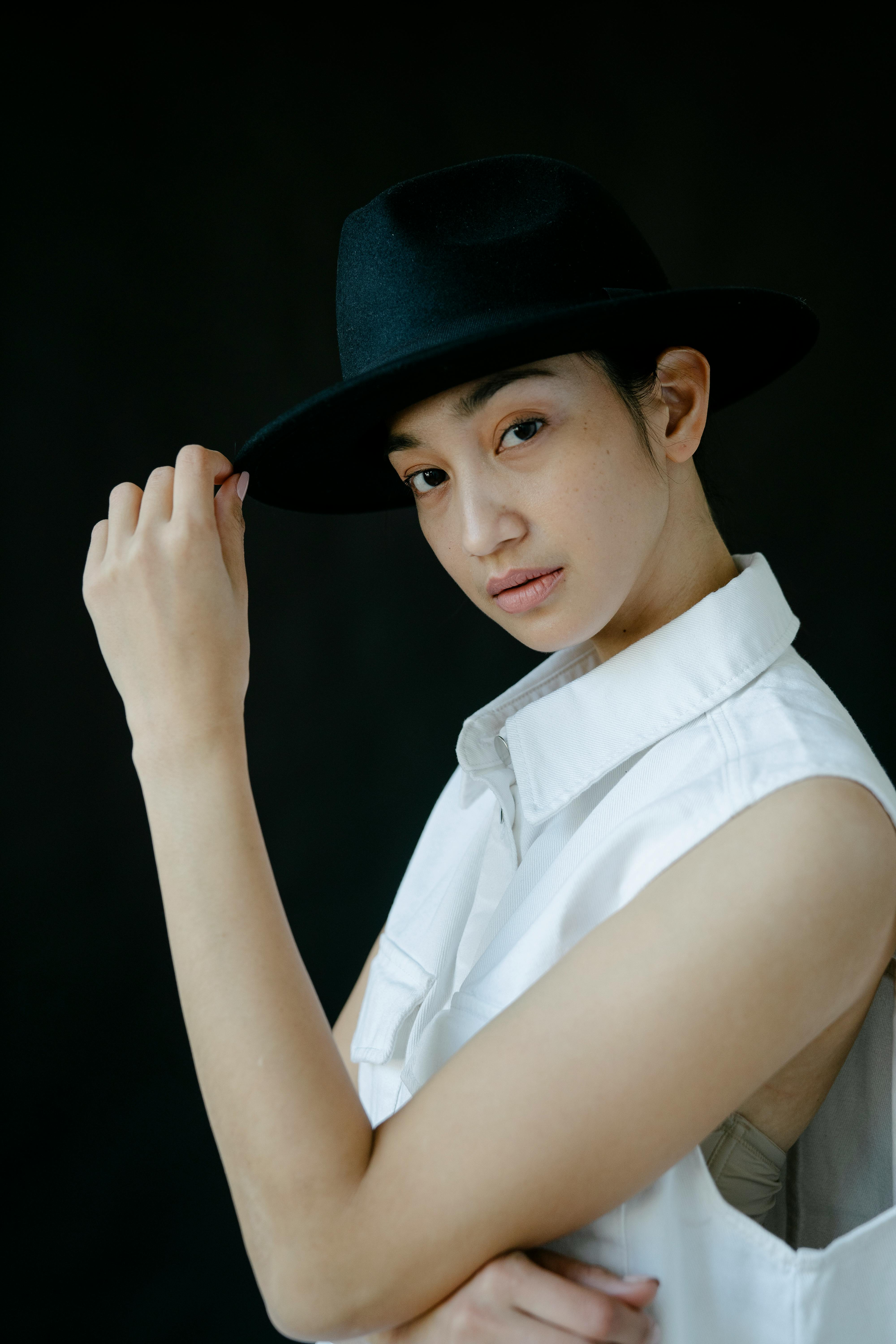 Sophisticated portrait of an Asian woman posing with a hat in a studio setting.