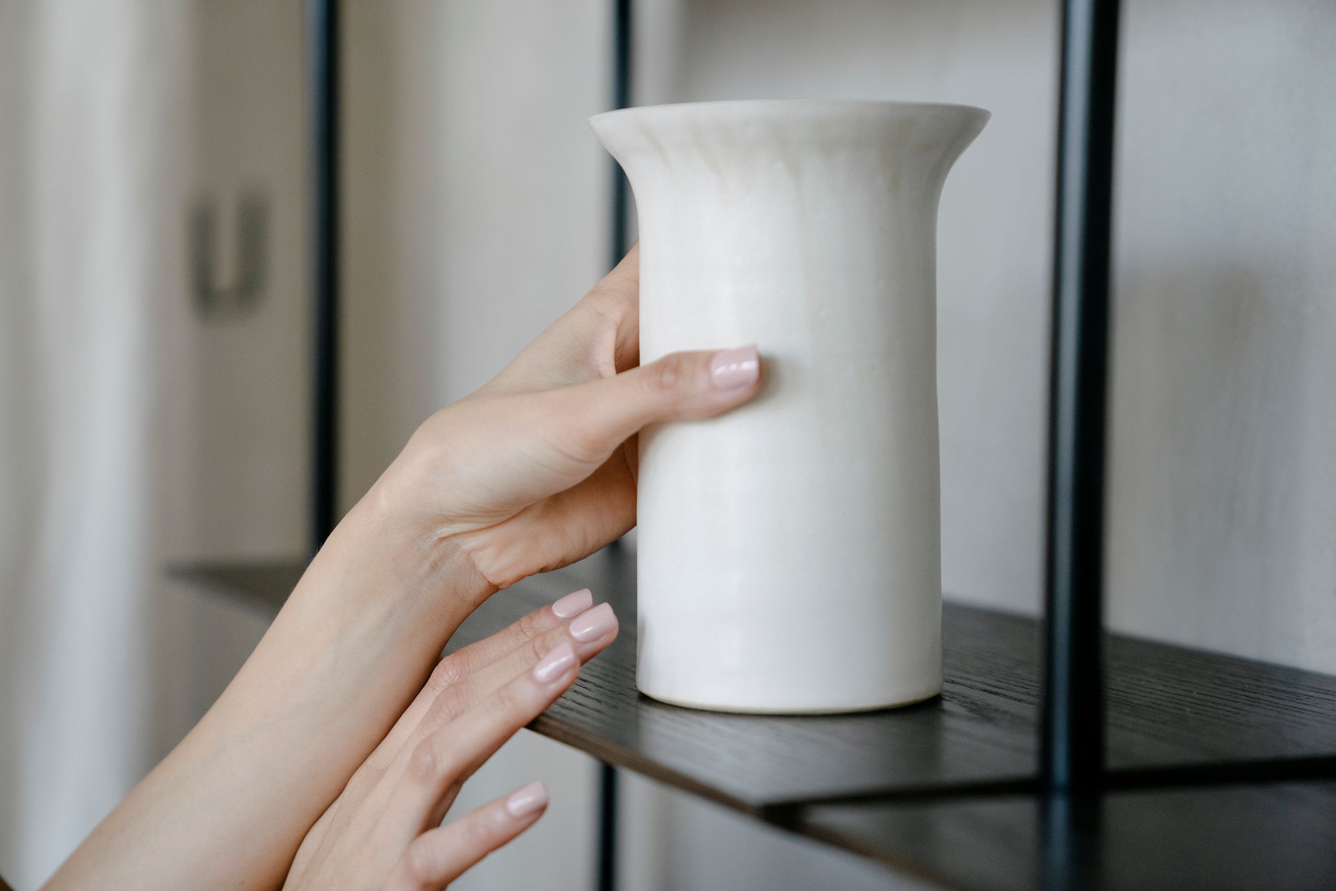 Close-up of woman's hands placing a ceramic vase on a modern wooden shelf indoors.