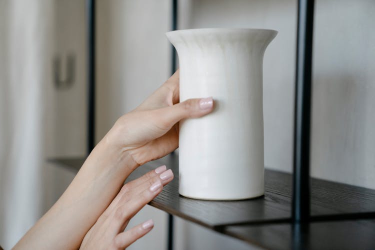 Close-up Of Woman Reaching For A Vase Standing On A Shelf 