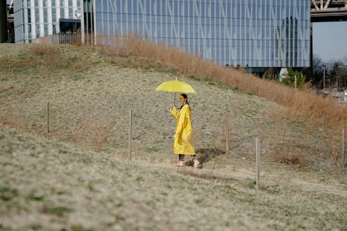 A Woman in Yellow Coat Walking while Holding a Yellow Umbrella