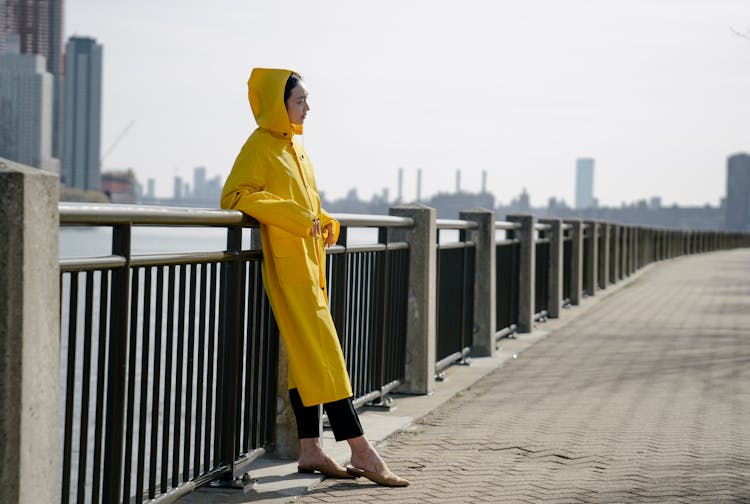 Woman In A Yellow Raincoat Standing On A Pier In City 