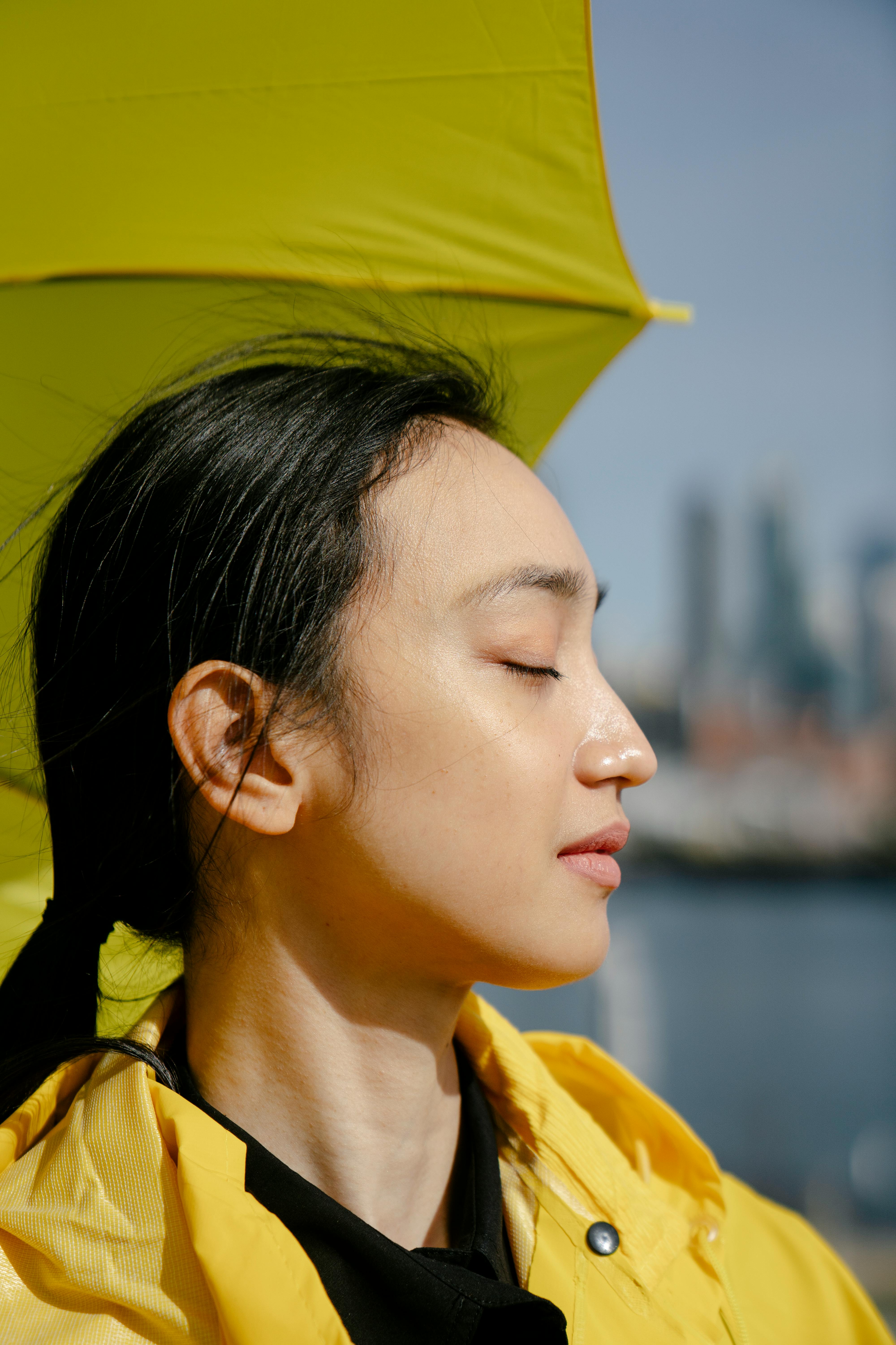 Profile of a woman with closed eyes holding a yellow umbrella outdoors.