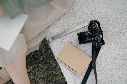 A notebook and a camera resting on a textured stone bench with soft light from above.