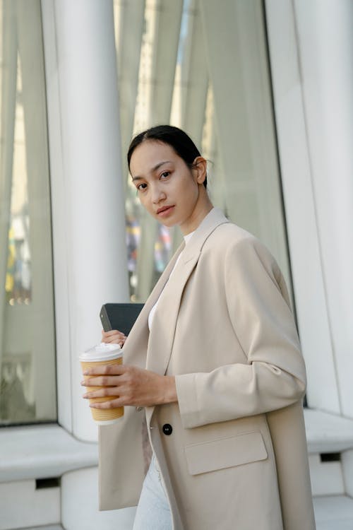 Free Elegant Woman in a Beige Blazer Holding a Coffee and Laptop  Stock Photo